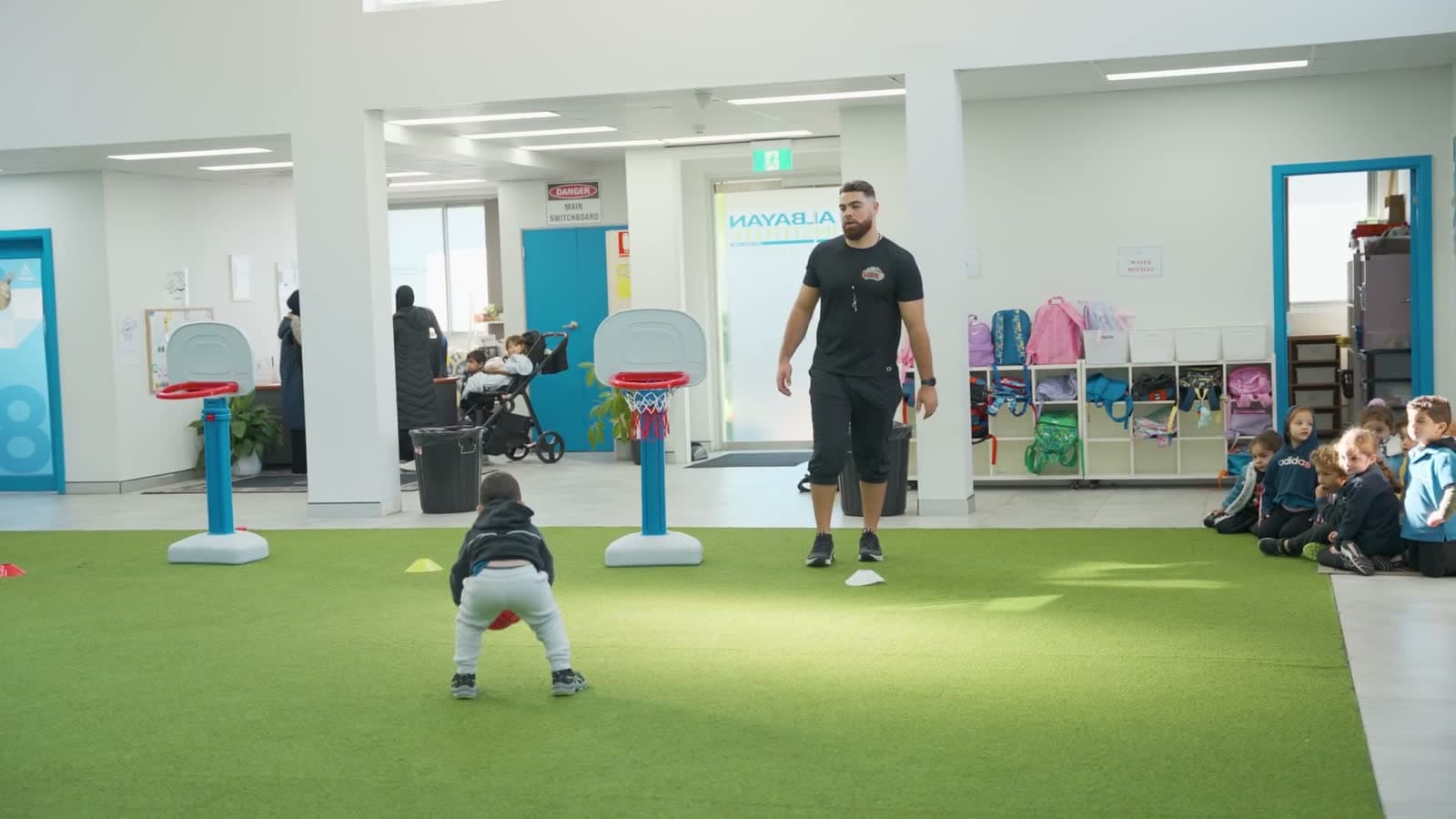 A Build Alpha Kids coach runs a ball-skills session with toddlers between mini hoops at a Sydney childcare centre