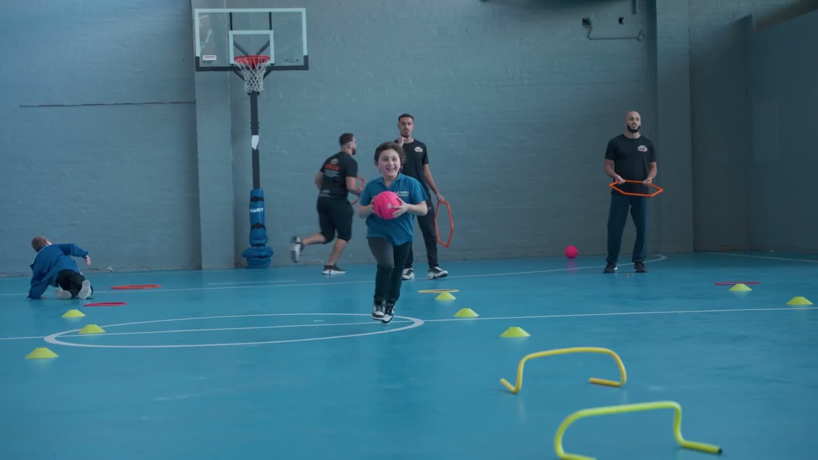 A student sprints with the ball through a Build Alpha Kids multi-sport school program, coaches running the drill behind